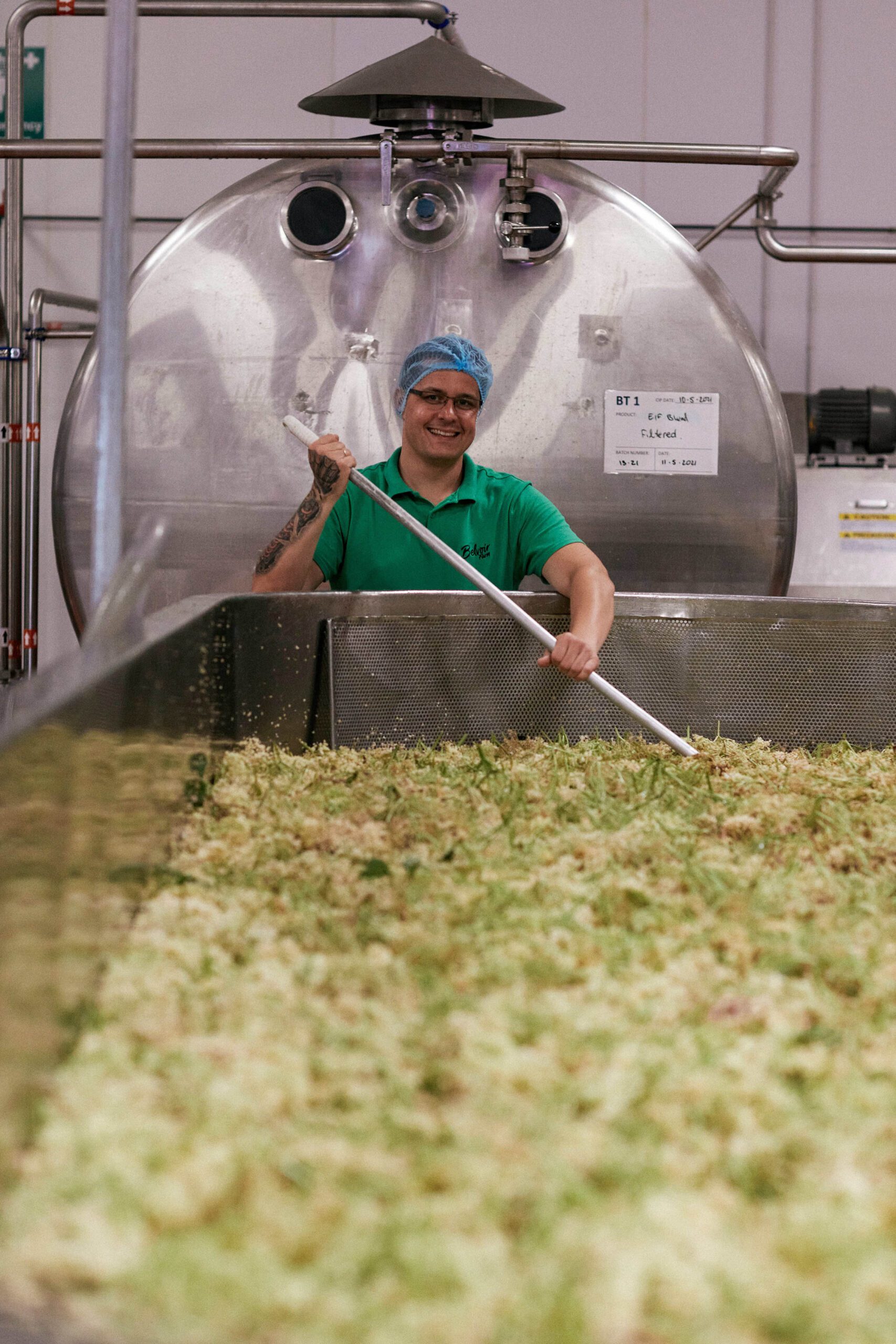 A Belvoir Farm team member working in the factory, hand stirring fresh elderflowers in a vat.